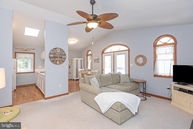 living area featuring baseboards, light carpet, ceiling fan, and vaulted ceiling