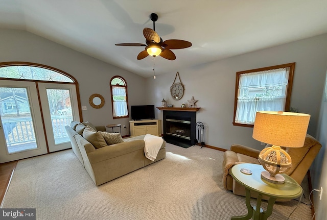 carpeted living area featuring baseboards, a fireplace with flush hearth, a ceiling fan, and vaulted ceiling