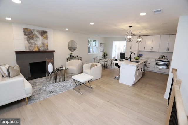 kitchen with visible vents, open floor plan, light wood-type flooring, stainless steel oven, and a sink