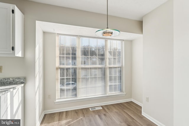 unfurnished dining area with wood finished floors, visible vents, and baseboards