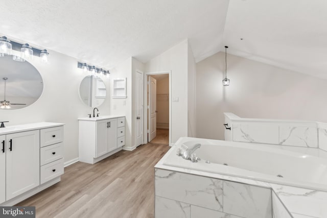 bathroom with two vanities, a sink, a textured ceiling, wood finished floors, and vaulted ceiling