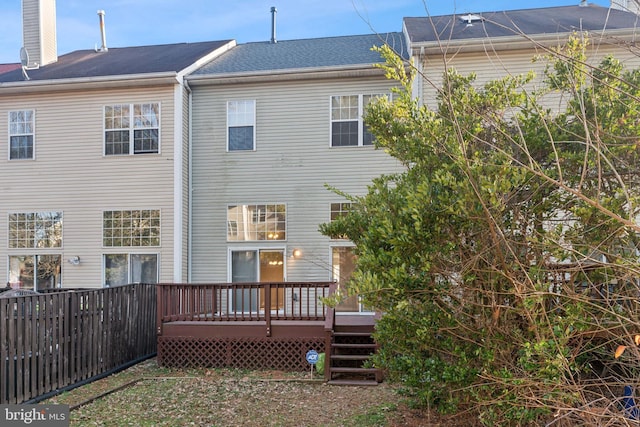 rear view of house featuring a wooden deck, a chimney, and fence