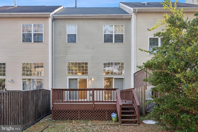 rear view of house with roof with shingles, a deck, and fence