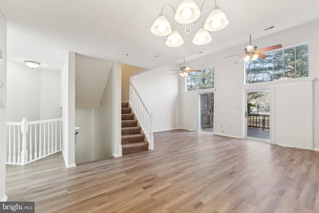 unfurnished living room with an inviting chandelier, light wood-style flooring, baseboards, and a towering ceiling