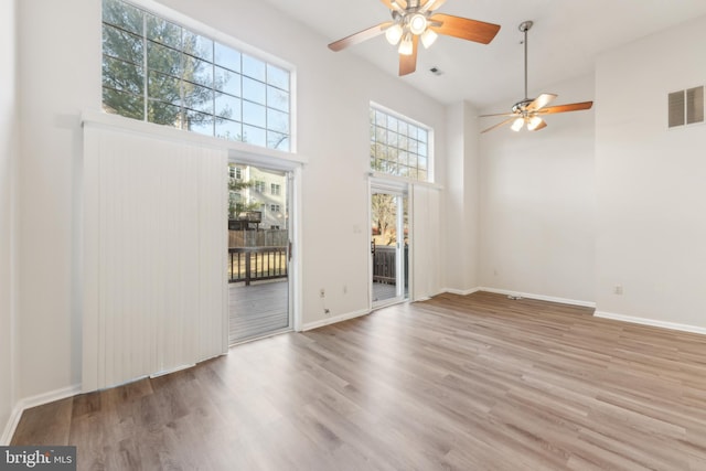 spare room with wood finished floors, visible vents, a towering ceiling, and baseboards