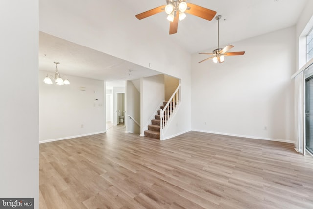 unfurnished living room with stairs, baseboards, light wood-type flooring, and a towering ceiling