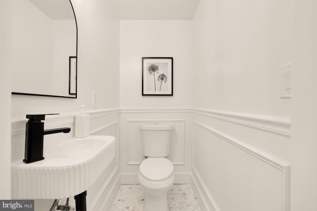 bathroom with a wainscoted wall, a sink, a decorative wall, and toilet