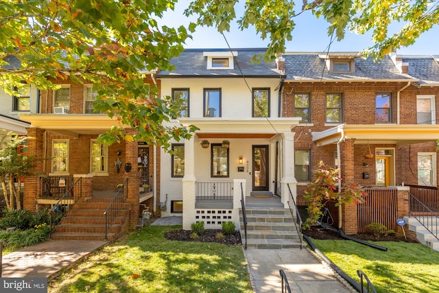 townhome / multi-family property featuring brick siding, mansard roof, a porch, a high end roof, and a front lawn