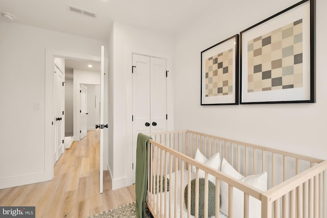 hall featuring light wood-type flooring, baseboards, visible vents, and an upstairs landing