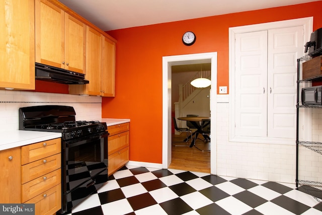 kitchen with tasteful backsplash, light countertops, black gas range oven, under cabinet range hood, and tile patterned floors