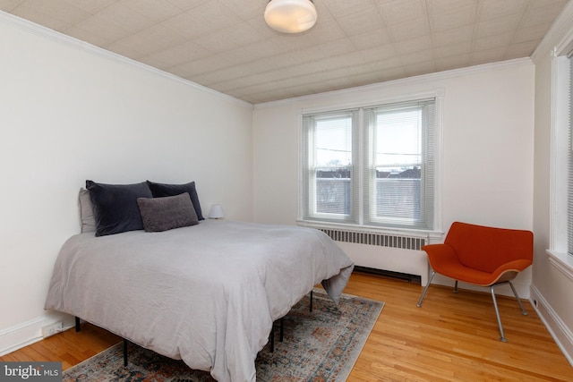 bedroom featuring radiator, light wood-style flooring, ornamental molding, and baseboards