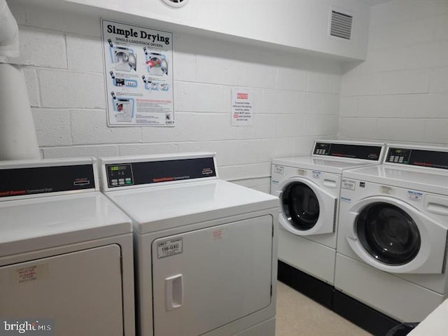 community laundry room featuring concrete block wall, visible vents, and separate washer and dryer