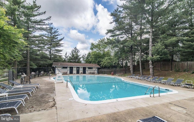 community pool featuring an outbuilding, a patio, and fence