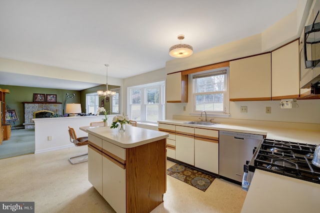 kitchen featuring light floors, light countertops, a stone fireplace, stainless steel dishwasher, and a sink