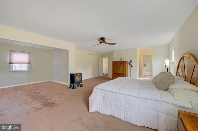 bedroom with baseboards, visible vents, carpet floors, a wood stove, and ceiling fan