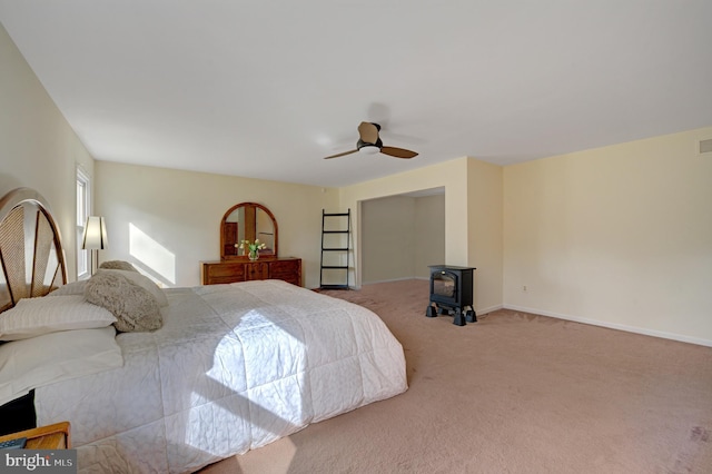 bedroom with baseboards, carpet floors, ceiling fan, and a wood stove