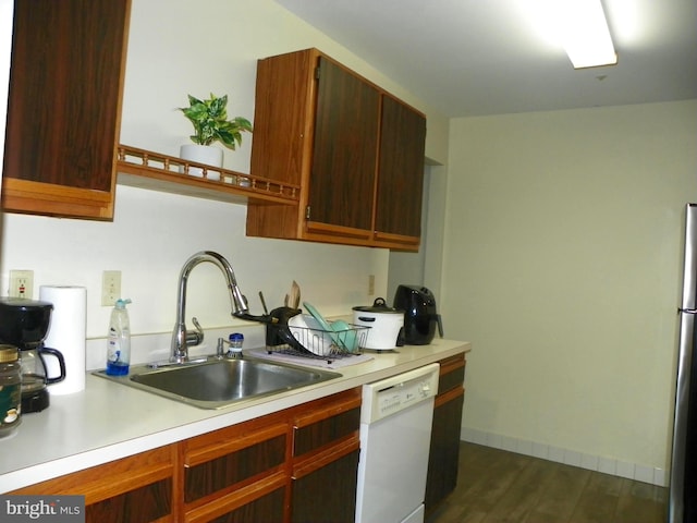 kitchen featuring light countertops, dark wood-type flooring, a sink, dishwasher, and baseboards