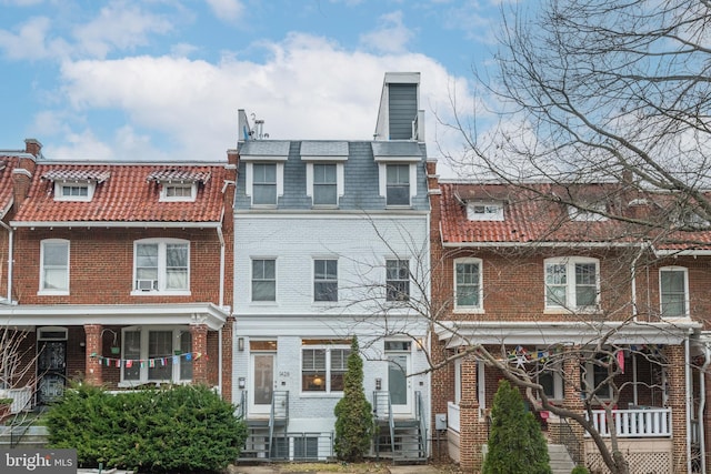 view of property featuring brick siding, mansard roof, a chimney, and entry steps