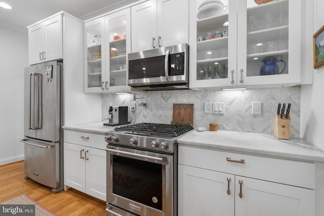 kitchen featuring light stone counters, white cabinetry, stainless steel appliances, and light wood-style floors