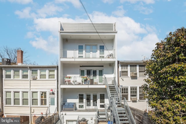 rear view of property featuring stucco siding, a balcony, stairs, and fence