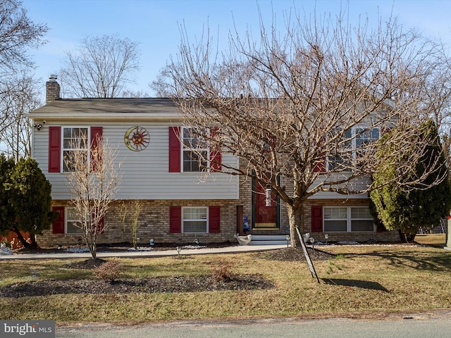 split foyer home featuring entry steps, a front yard, brick siding, and a chimney