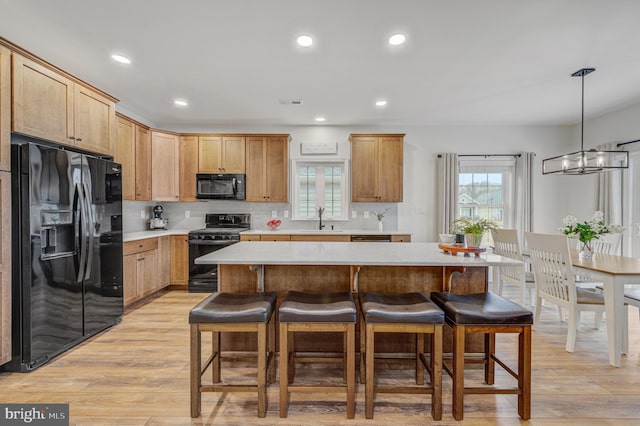 kitchen featuring a breakfast bar, black appliances, light countertops, and light wood-type flooring