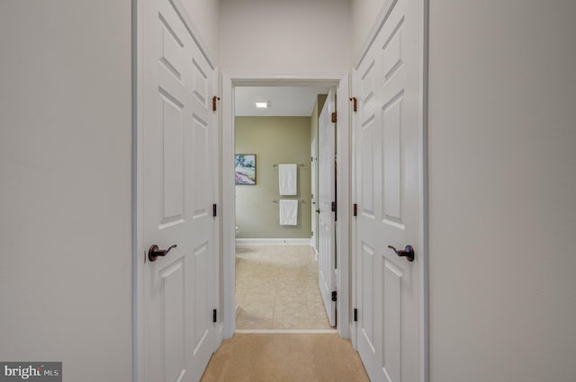 hall featuring baseboards and light colored carpet