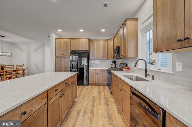 kitchen featuring a sink, black appliances, light countertops, light wood-style floors, and backsplash