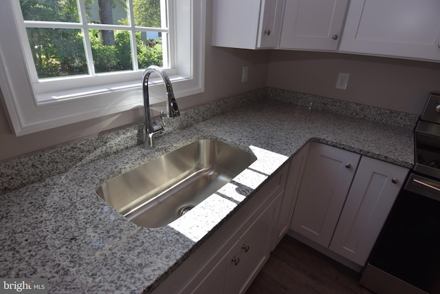 kitchen with dark wood finished floors, white cabinets, stove, light stone countertops, and a sink