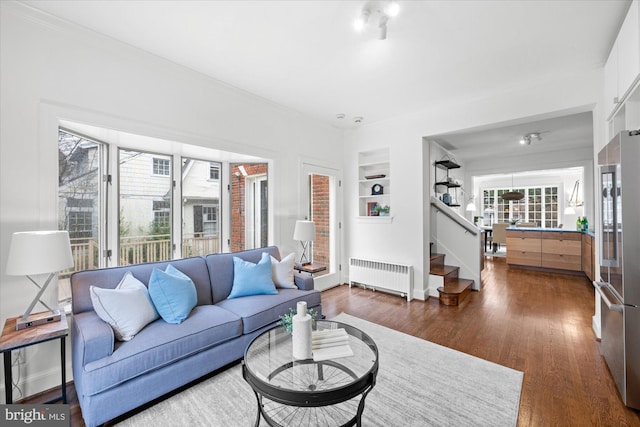 living area with built in shelves, wood finished floors, baseboards, stairway, and radiator