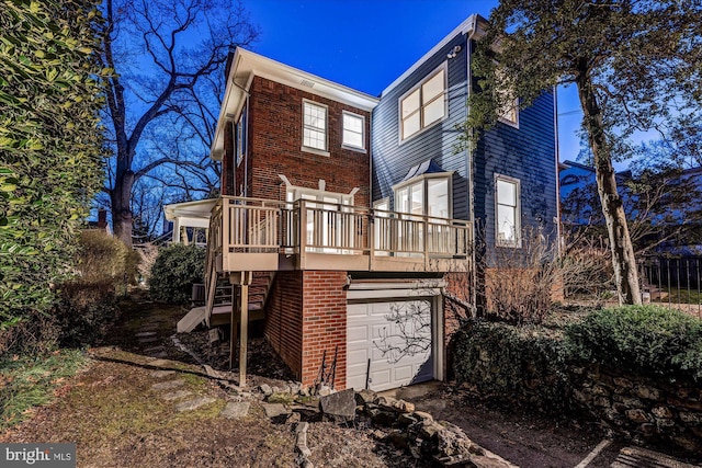 rear view of house featuring a garage, brick siding, stairway, and a deck