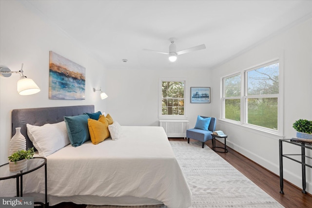 bedroom with radiator, ceiling fan, baseboards, and wood finished floors