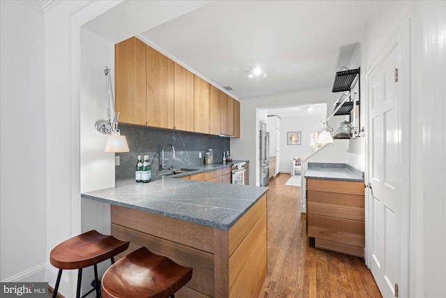 kitchen with wood finished floors, high end refrigerator, a sink, and decorative backsplash