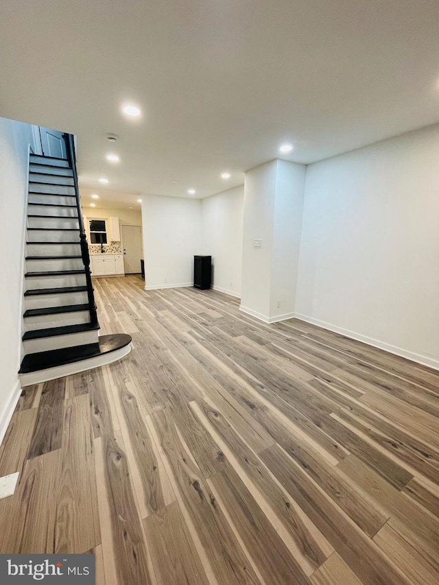 finished below grade area featuring recessed lighting, stairway, baseboards, and wood finished floors