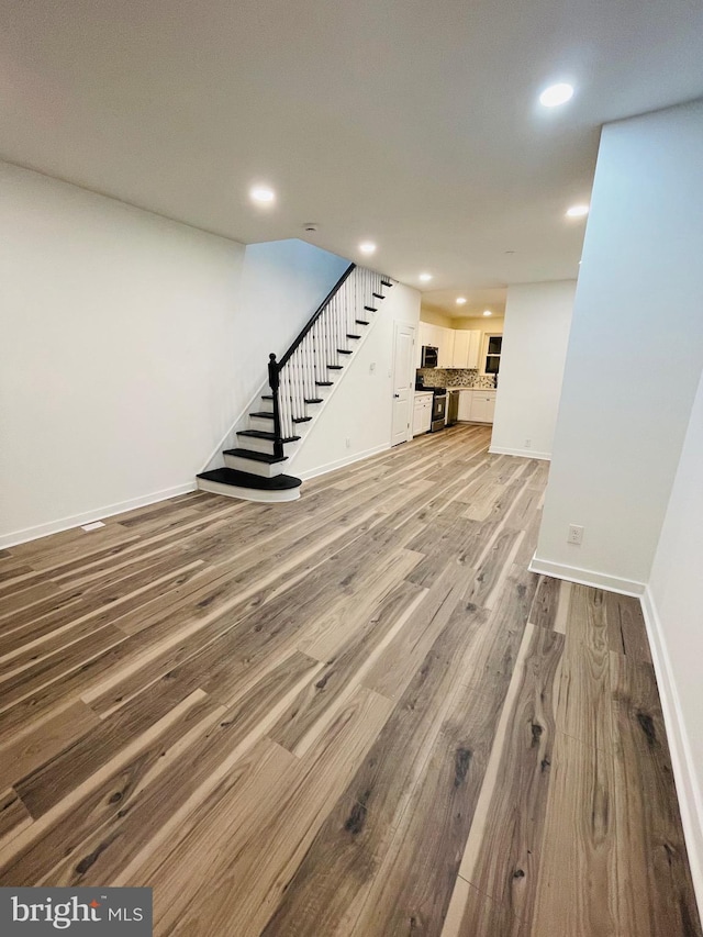 unfurnished living room featuring light wood-style flooring, stairway, baseboards, and recessed lighting