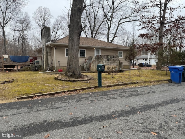 single story home featuring a wooden deck, a chimney, a front lawn, and roof with shingles