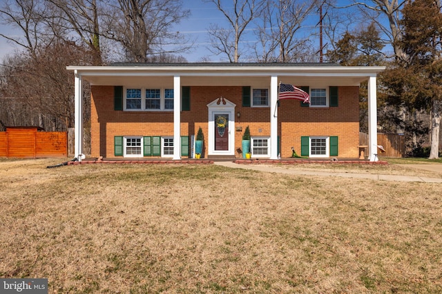 raised ranch with brick siding, a front lawn, and fence