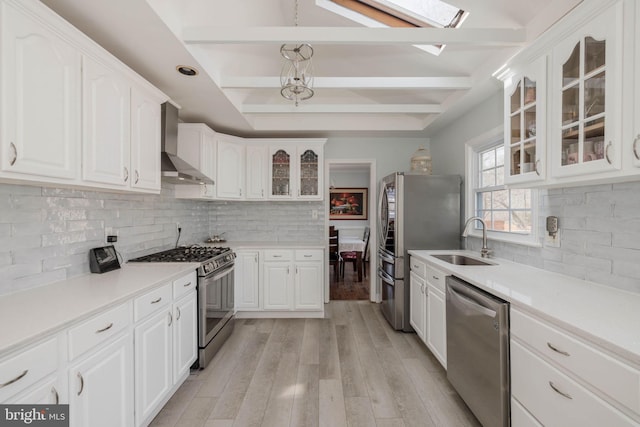 kitchen with appliances with stainless steel finishes, light wood-style floors, white cabinets, a sink, and wall chimney exhaust hood