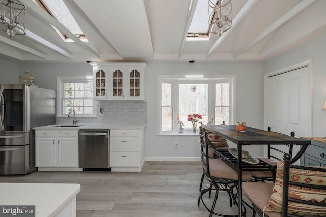 kitchen featuring light wood-style flooring, stainless steel appliances, a sink, light countertops, and glass insert cabinets