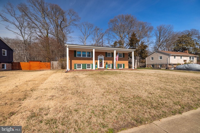 split foyer home featuring brick siding, a porch, a front yard, and fence