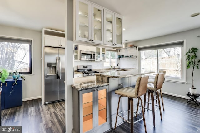 kitchen with a wealth of natural light, appliances with stainless steel finishes, white cabinets, and light stone counters