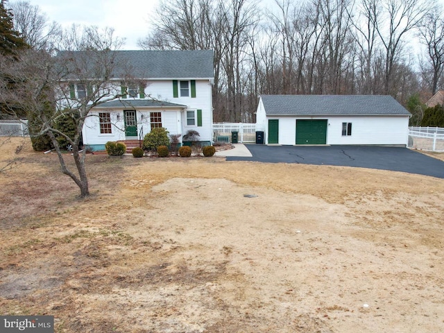 view of front of home with roof with shingles, a detached garage, fence, and an outbuilding