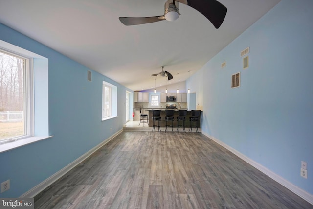 unfurnished living room featuring dark wood-style floors, plenty of natural light, visible vents, and vaulted ceiling