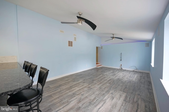 interior space with ceiling fan, wood finished floors, visible vents, baseboards, and vaulted ceiling