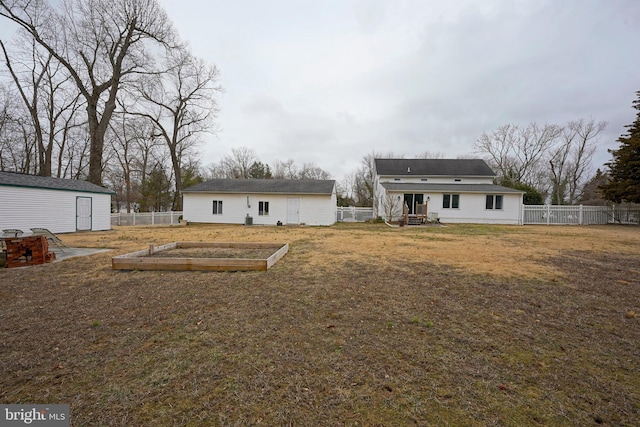 back of property with a vegetable garden, fence, an outdoor structure, and a lawn