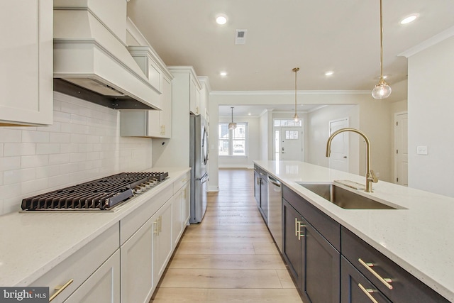 kitchen featuring stainless steel appliances, a sink, white cabinetry, custom exhaust hood, and crown molding