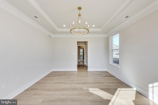 spare room featuring an inviting chandelier, ornamental molding, a raised ceiling, and light wood-style floors