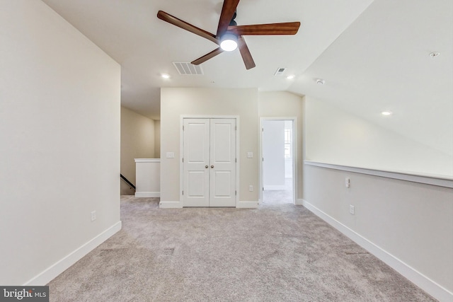 carpeted spare room with a ceiling fan, visible vents, vaulted ceiling, and baseboards