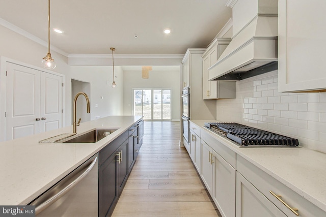 kitchen featuring light wood finished floors, tasteful backsplash, appliances with stainless steel finishes, custom exhaust hood, and a sink