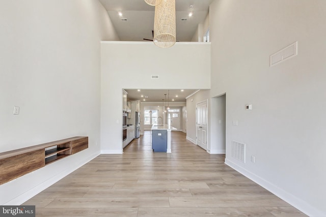 unfurnished living room with a chandelier, light wood-type flooring, a sink, and visible vents